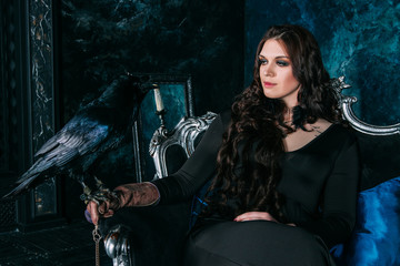 Fototapeta na wymiar young beautiful caucasian woman with black raven on her hand sitting on sofa