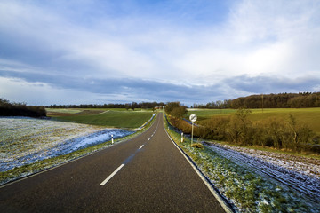 Empty black asphalt road between green fields