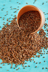 Flax seeds in a clay bowl isolated on blue background, close-up, selective focus, vertical.