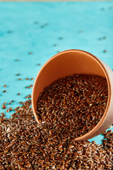 Flax seeds in a clay bowl isolated on blue background, close-up, selective focus, vertical.