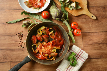 tagliatelle with artichoke and tomato sauce in the pan with ingredients around