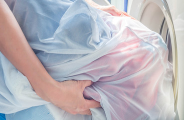 Closeup of woman 's hand. Putting dirty clothes in laundry bags into washing machine.