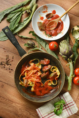 tagliatelle with artichoke and tomato sauce in the pan with ingredients around