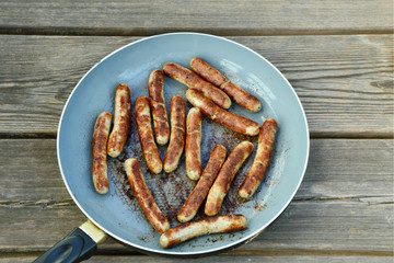 Grilled sausage cooked in pan on wooden background