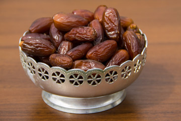 Dates fruit on a silver bowl on wooden table. The Muslim feast of the holy month of Ramadan Kareem
