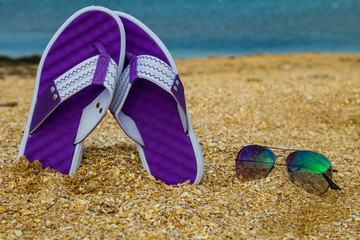 Pair of flip flops and sunglasses on a sandy sea beach