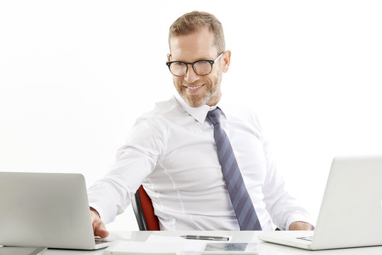 Middle Aged Business Man Portrait. Successful Smiling Businessman Sitting At Desk With Laptops And Working. Isolated On White Background.  