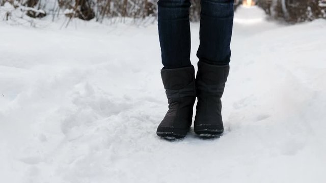 Close-up of the frozen legs of a woman in boots in the snow stomping from the cold.