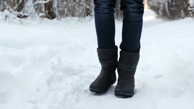 Close-up of the frozen legs of a woman in boots in the snow stomping from the cold.