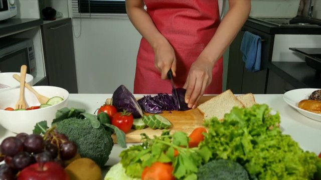 close up of happy woman woman cutting purple cabbage in kitchen room at home