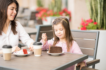 Little girl having cake with mother at cafe