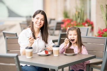 Beautiful mother and daughter having cake at cafe