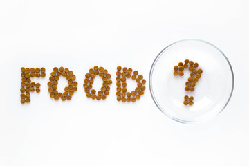 Word FOOD and question mark made of dry cat or dog food with empty bowl. Pet care and veterinary concept with letters on white background.