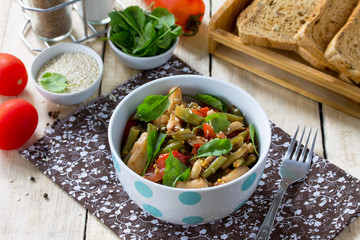 Healthy vitamin dinning bowl on the kitchen wooden table. Warm salad with chicken, green beans, arugula, tomatoes and sauce of salad dressing.