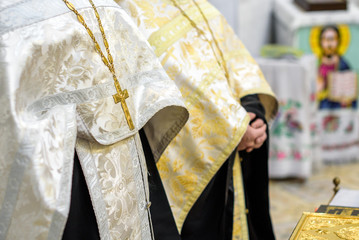 Beautiful golden cross in male hands of priest wearing gold robe on ceremony in christian cathedral...