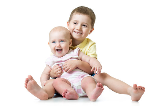 Portrait of kid brother hugging his little cute sister sitting on floor isolated on white background