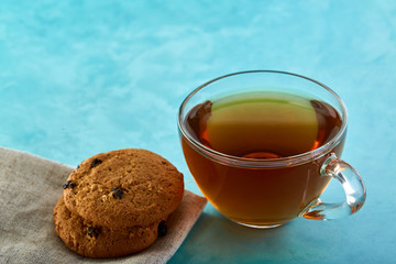 Glass cup of tea and oatmeal chocolate cookies close-up on blue background.