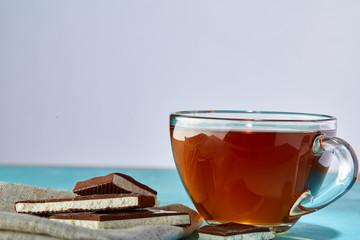 Glass cup of tea and chocolate close-up on blue background.