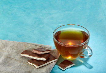 Glass cup of tea and chocolate close-up on blue background.