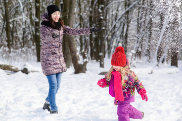 Fototapeta na wymiar Mother and daughter play snowballs in winter forest