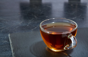 Glass cup of tea isolated on dark marble background, close-up