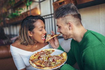 Mixed race couple eating pizza in modern cafe. They are laughing and eating pizza and having a great time.