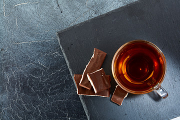 glass cup of black tea with chocolate pieces on a dark greyish marble background. Top view