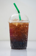 iced cola in plastic transparent cup with green straw on white background with shadow