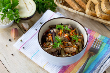 Warm salad with boiled meats and grilled vegetables (eggplant, carrots, paprika) он the kitchen wooden table.