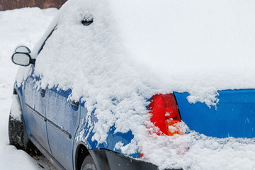 The blue car is covered with snow after snowfall.