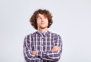 Fototapeta na wymiar A curly-haired guy thinks with a serious emotion on a gray background.