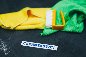 Cleaning house or office concept. Green and yellow rags, cleaning brush, cleantastic inscription on a dark concrete background. Top view, closeup