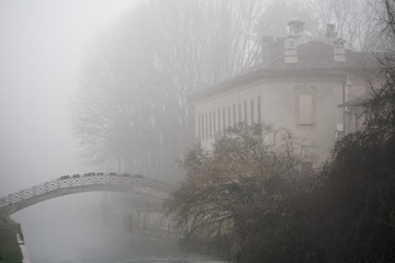 Old Arch stone bridge in foggy weather, haze winter in Italy