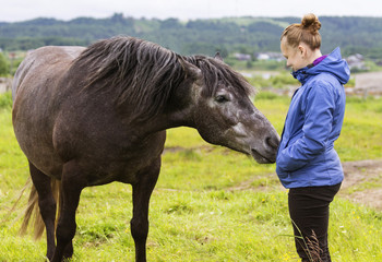 It is natural horsemanship, the young girl is taming a feral black horse. The tamer is working with a bronco based on the gentle animal training method. The human is communicating with a mare.