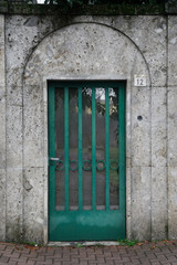 Steel green door with a grid embedded in a massive concrete stone wall Straightforward style