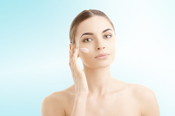 Studio shot of beautiful young woman applying moisturizer cream onto her face against at isolated...
