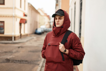 handsome young man in a fashionable sports jacket with a cap with a black backpack walking outdoors in the city © alones