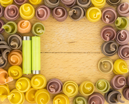 Multicolored pasta and two batteries. The concept of energy in food. on a wooden background.