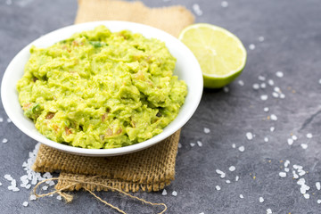 Bowl of guacamole on black wooden background.