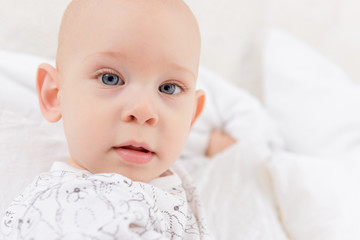 Adorable baby boy with blue eyes looking directly at camera trying to reach for it. Cute toddler close up portrait.