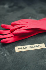 Cleaning house or office concept. Cleaning red rubber glives, AAAH, CLEAN inscription on a dark concrete background. Top view, closeup - obrazy, fototapety, plakaty