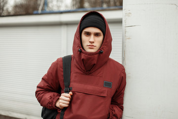 Fashionable young man in a sporty fashion jacket with a hat and a black bag near a white wall on the street © alones