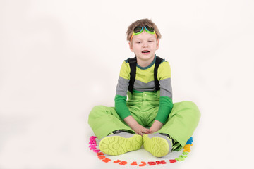 Happy charming Caucasian blond kid in colored clothes playing with plastic letters. Learning the alphabet, preparing for school. Education for kindergarten and preschool children. White background