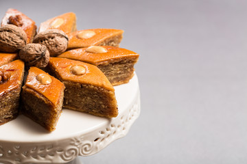 Traditional pakhlava baklava pastry from Azerbaijan made of walnuts and almonds with honey in round white plate cake stand on grey background, Novruz eastern new year spring celebration concept 