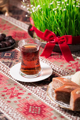 Novruz setting table decoration, tea in  tulip shape glass on ethnic motives rustic table cloth with wheat grass, dyed eggs, traditional sweets, samovar, new year sring celebration, nature awakening