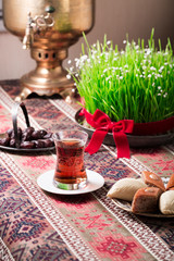 Novruz setting table decoration, tea in  tulip shape glass on ethnic motives rustic table cloth with wheat grass, dyed eggs, traditional sweets, samovar, new year sring celebration, nature awakening