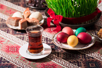 Novruz setting table decoration, tea in  tulip shape glass on ethnic motives rustic table cloth with wheat grass, dyed eggs, traditional sweets, samovar, new year sring celebration, nature awakening