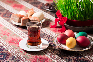 Novruz setting table decoration, tea in  tulip shape glass on ethnic motives rustic table cloth with wheat grass, dyed eggs, traditional sweets, samovar, new year sring celebration, nature awakening