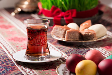 Novruz setting table decoration, tea in  tulip shape glass on ethnic motives rustic table cloth with wheat grass, dyed eggs, traditional sweets, samovar, new year sring celebration, nature awakening