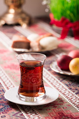 Novruz setting table decoration, tea in  tulip shape glass on ethnic motives rustic table cloth with wheat grass, dyed eggs, traditional sweets, samovar, new year sring celebration, nature awakening